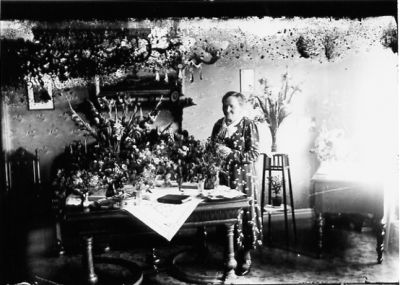 Kvinna stående i rum med blommor.
Nyckelord: Blommor Lampa Pedistal