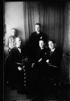 3 män sittande och 2 stående i rum.
