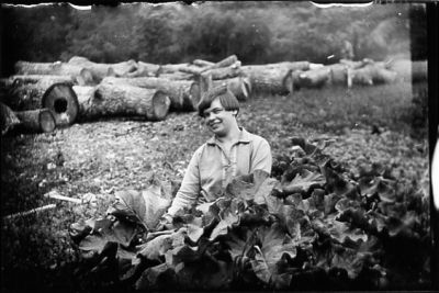 Kvinna sittande på backen framför stockar.
Nyckelord: Timmer