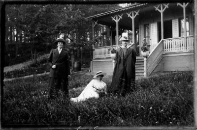 2 kvinnor stående och 1 kvinna sittande i gräset framför byggnad.
Nyckelord: Servering Veranda