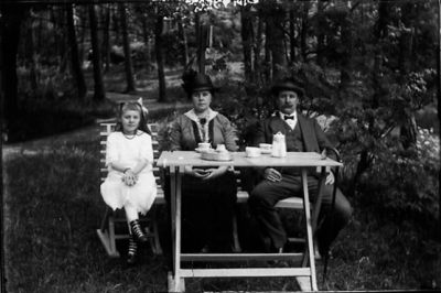 Man, kvinna och flicka sittande vid trädgårdsmöbel.
Nyckelord: Trädgårdsmöbel Kaffe