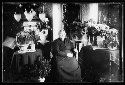 Kvinna sittande i rum med blommor.
Nyckelord: Blommor Lampa