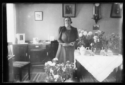 Kvinna stående i rum bland blommor.
Nyckelord: Blommor Klocka Tavla