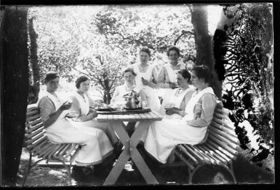 5 kvinnor sittande och 2 stående vid trädgårdsmöbel. Alla med uniform.
Nyckelord: Trädgårdsmöbel Kaffe Uniform