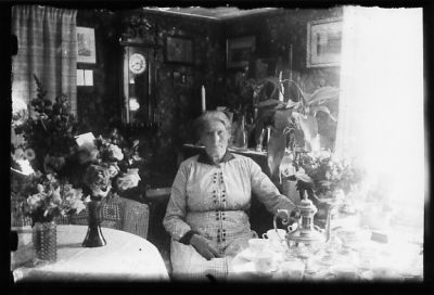 Kvinna sittande i rum med kaffe och blommor.
Nyckelord: Blommor Kaffe Klocka Tavla