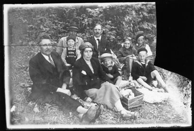 2 män, 2 kvinnor och 5 barn sittande i gräset med picnickorg.
Nyckelord: Picnickorg