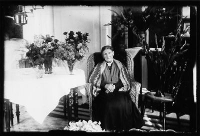 Kvinna sittande i rum bland blommor.
Nyckelord: Blommor