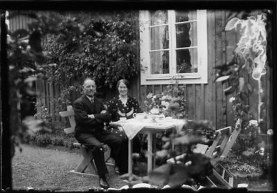 Man och kvinna sittande vid kaffebord framför byggnad.
Nyckelord: Trädgårdsmöbel Kaffe