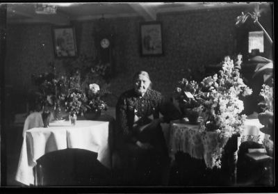 Kvinna sittande i rum bland blommor.
Nyckelord: Blommor Klocka Tavla