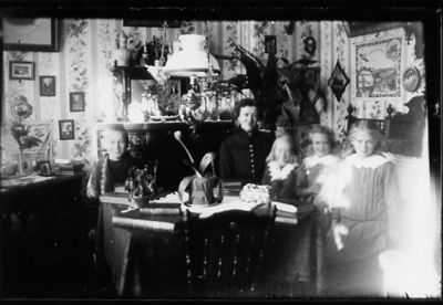 Kvinna, pojke och 3 flickor sittande i rum.
Nyckelord: Lampa
