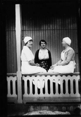Kvinna stående och 2 kvinnor sittande på verandaräcke.
Nyckelord: Veranda Räcke