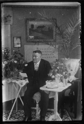 Man sittande i rum med blommor.
Nyckelord: Bord Tavla Blommor