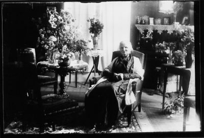 Kvinna sittande i rum med blommor.
Nyckelord: Blommor