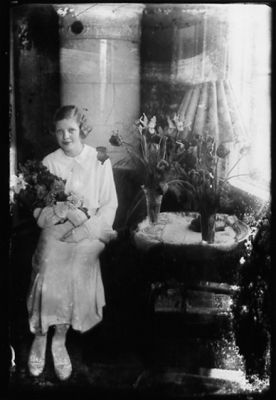 Kvinna sittande i rum med blommor i knät.
Nyckelord: Kakelugn Blommor