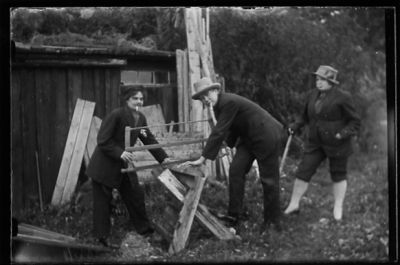 Man och kvinna sågar på sågbock och kvinna står och tittar på.
Nyckelord: Såg Sågbock