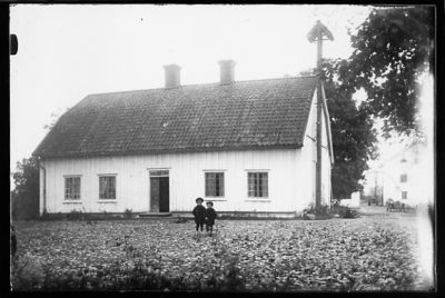 2 barn stående framför byggnad.
