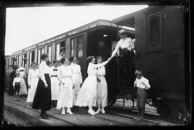 Ett antal personer stående vid eller på järnvägsvagn.
Nyckelord: Järnvägsvagn Perrong