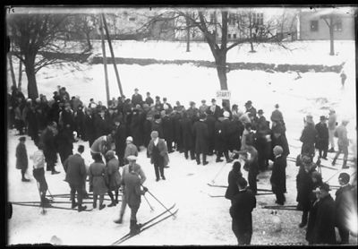 Ett antal personer stående i snön, en del med skidor på.
Nyckelord: Skidor
