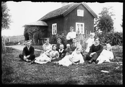 Ett antal personer sittande på gräsmatta framför byggnad.
