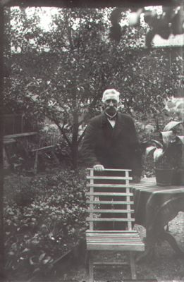 Man stående i trädgård.
Nyckelord: Stol Växtlighet