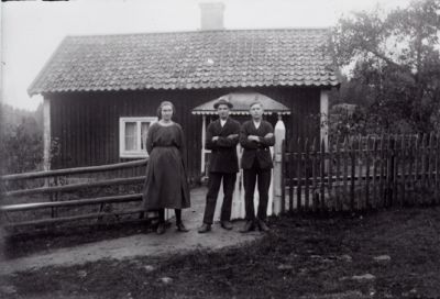 2 män och 1 kvinna stående framför grind till tomt.
Nyckelord: Grind