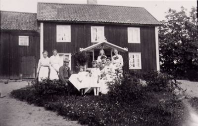 2 män, 5 kvinnor och 2 barn på gräsmatta framför byggnad.

