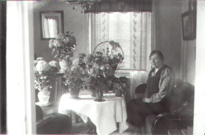 Kvinna sittande i soffa med blombord framför sig.
Nyckelord: Blommor