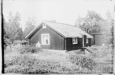 Kvinna stående framför byggnad.
Nyckelord: Trädgård