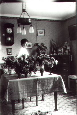 Kvinna stående vid bord med blommor.
Nyckelord: Blommor Klocka Lampa