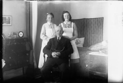 Man sittande på stol och 2 kvinnor sytående bakom.
Nyckelord: Byrå Fickur Uniform