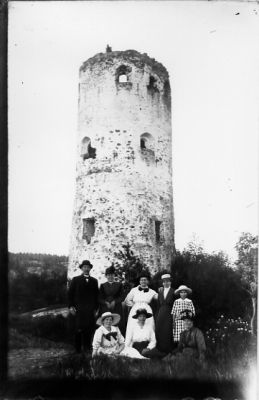 Man och 7 kvinnor framför ruin.
