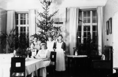 3 kvinnor stående och 2 sittande framför julgran.
Nyckelord: Julgran Uniform