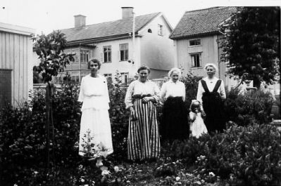 4 kvinnor och 1 flicka stående i trädgård.
Nyckelord: Trädgård