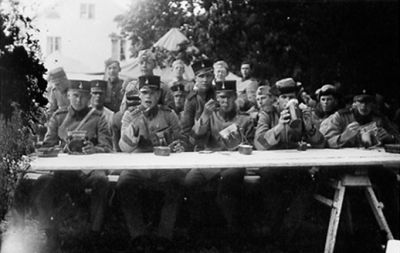 Ett antal uniformklädda män sittande och äter.
Nyckelord: Militär Tält Mattonister