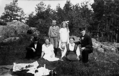 2 män och 2 kvinnor sittande och pojke och flicka stående i skogsbacke.
Nyckelord: Skogsbacke Picnic