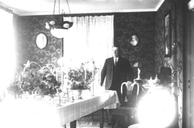 Man stående vid bord med blommor.
Nyckelord: Blommor Tapet Lampa