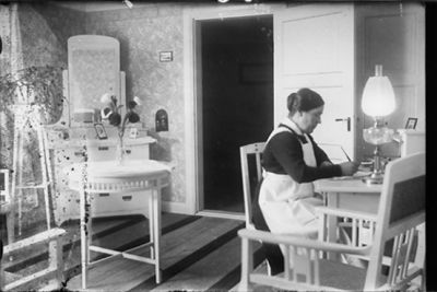 Kvinna sittande vid skrivbord.
Nyckelord: Skrivbord Lampa Spegel