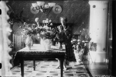 Kvinna stående vid bord med blommor i finrum.
Nyckelord: Födelsedag Lampa Blommor Matta