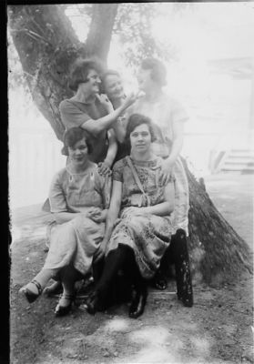 3 kvinnor stående och 2 kvinnor sittande framför träd.
Nyckelord: Träd