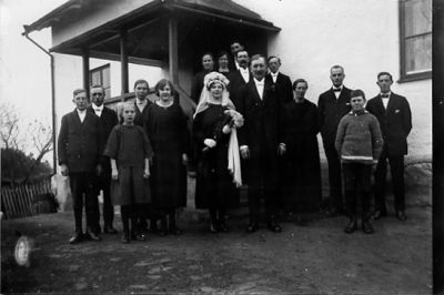 Bröllopsfölje samlade framför byggnad.
