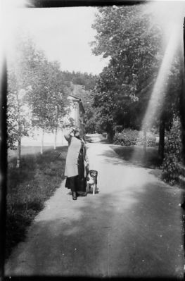 Kvinna stående med hund på grusgång.
Nyckelord: Hund Grusgång Byggnad