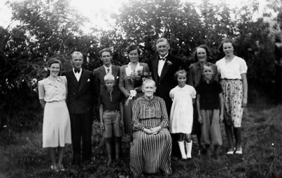 3 män, 4 kvinnor, 2 pojkar och 1 flicka stående med 1 kvinna sittande framför, i trädgård.
Nyckelord: Trädgård