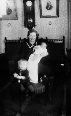 Kvinna sittande med barn i knät och bredvid barn sittande i fotölj.
Nyckelord: Klocka Tavla