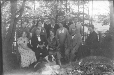 3 män och 4 kvinnor stående och 2 män och 3 kvinnor sittande framför staket.
Nyckelord: Hund Staket