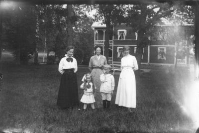 3 kvinnor, 1 pojke och 1 flicka stående på gräsmatta framför byggnad.
Nyckelord: Gräsmatta Park