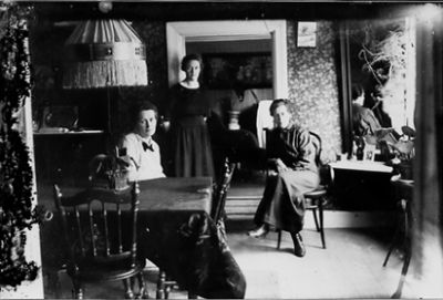 Kvinna stående och 2 kvinnor sittande i rum.
Nyckelord: Dörröppning Lampa