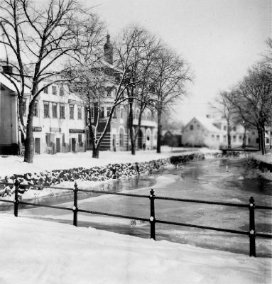 Vinterbild av byggnader utmed vattendrag
