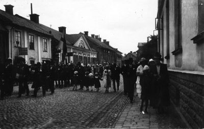 Ett antal personer som tågar på kullerstensbelagd gata
Nyckelord: Kullersten