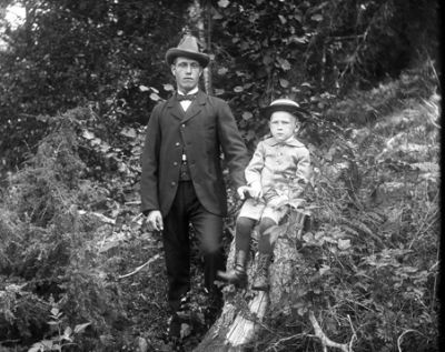 Stående man och pojke sittande på stubbe
Nyckelord: Kostym Hatt Kängor