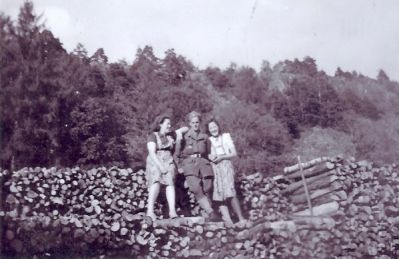 Militär omgiven av 2 flickor stående vid vedtrave
Nyckelord: Uniform Vedtrave